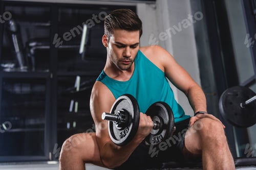 Preview: strong muscular sportsman lifting dumbbell in gym