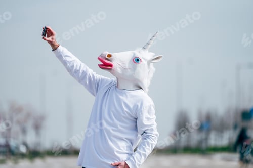 Preview: Man wearing unicorn mask taking a photo with smartphone