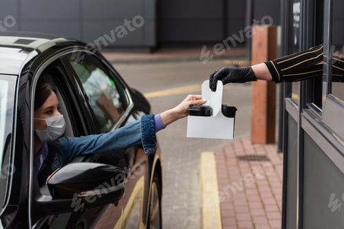 Preview: seller giving takeaway drink to woman in car wearing medical mask