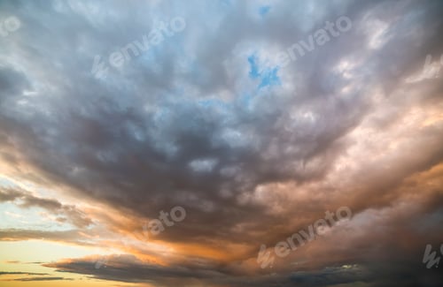 Preview: Beautiful view of dark blue clouds lit by bright orange yellow sun on clear sky.