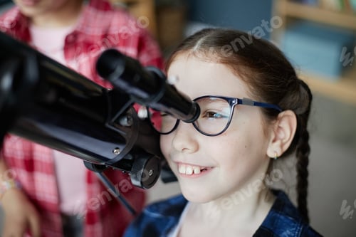 Preview: Caucasian Girl Smiling While Observing through Telescope Indoors