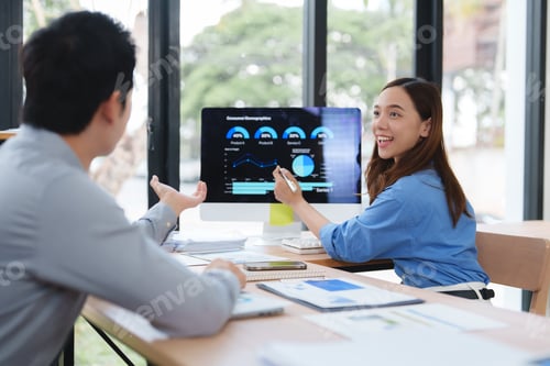 Preview: Businesswoman showing business chart on computer screen to businessman in office