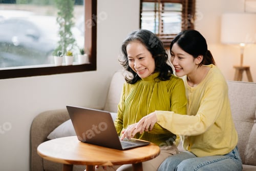 Preview: Happy adult granddaughter and senior grandmother having fun enjoying talk sit on sofa in modern
