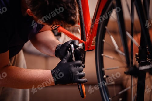 Man Adjusting Orange Bicycle with Tool Wearing Gloves