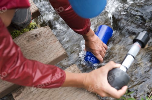 Preview: Female hiker with water filter filling water bottle in stream