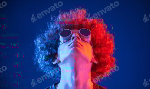 Preview: Portrait of young man with curly hair that is indoors illuminated by neon lighting. In retro eyewear