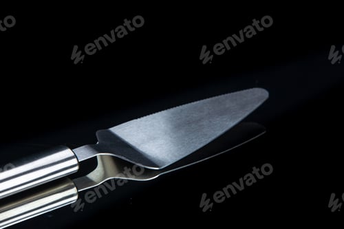 Preview: Close up view of kitchen stainless cake slicer lying on the right side on black background with