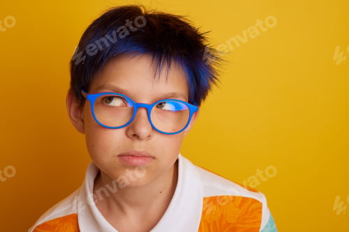 Preview: teenager boy with glasses looks away in surprise on isolated on light yellow background