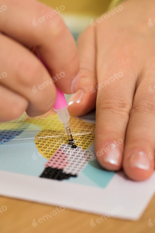 Preview: A close-up of a hand placing crystals on a canvas for a diamond painting project. Diamond Mosaic