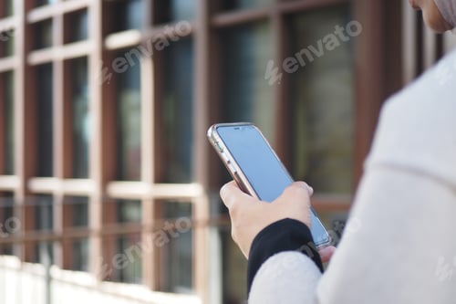 Preview: Person using smartphone while standing near modern building exterior