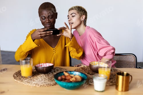 Preview: Two multiracial girls having breakfast, laughing, talking and looking in phone