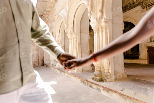 Preview: Loving couple walking hand in front of the columns and majestic arches of Orchha Fort in India