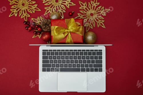 Preview: Top view of laptop near wrapped gift and decorations on red background
