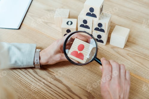 Preview: cropped view of woman holding magnifier near wooden cube