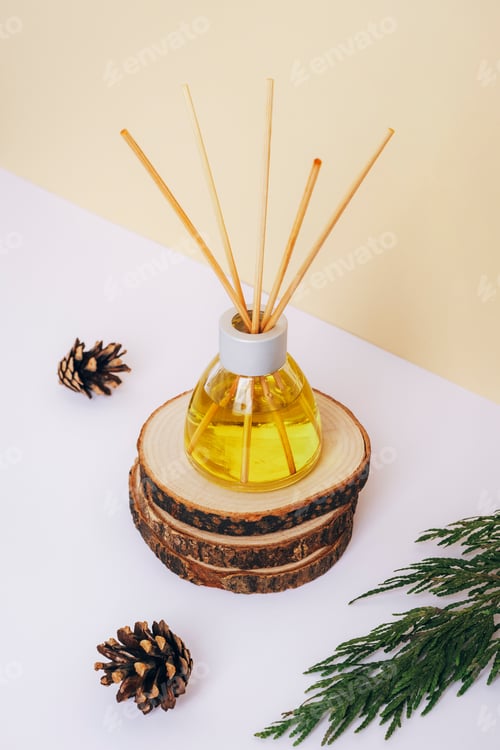 Preview: Glass bottle of aroma diffuser and pine cones on wooden stand on a white table. Close up.