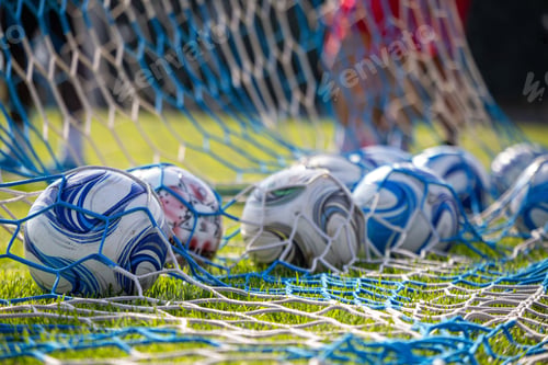 Preview: Soccer ball on field. Behind view of net and football ball on green grass. Blur team background.