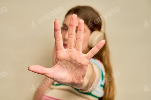 Preview: Young woman making stop sign with hand and listening music with headphones