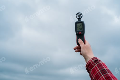 Preview: a farmer holds in his hand an instrument for measuring wind speed against the background of the sky