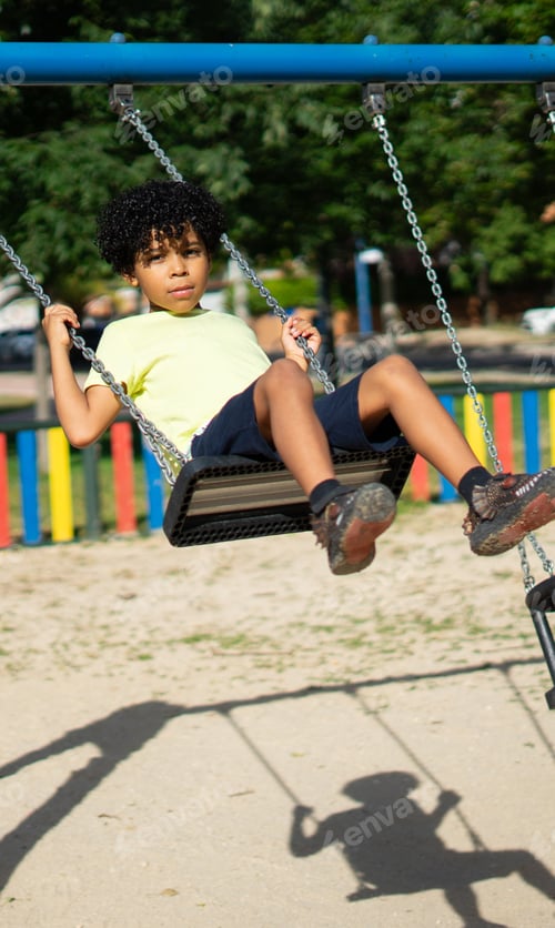 Preview: Latino boy with afro hair swinging on a playground swing