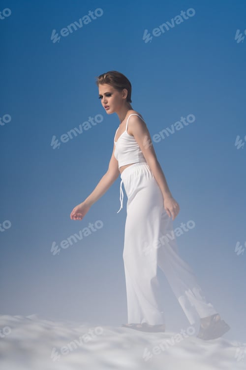 Preview: Beautiful European female tourist walking through snow with light fog on sunny day with blue sky