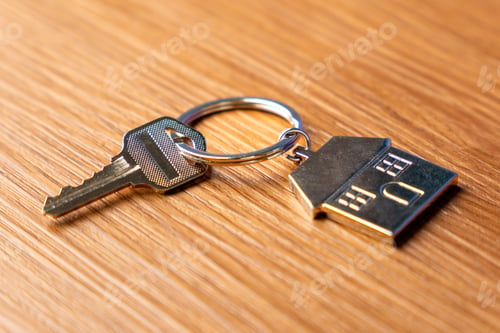 Preview: A key attached to a metallic house-shaped keychain on a table.