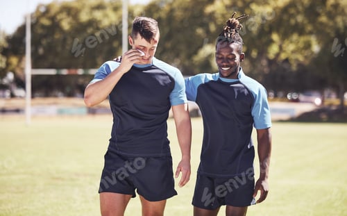 Preview: Two diverse young rugby players standing outside on the field. Black man smiling while talking to h