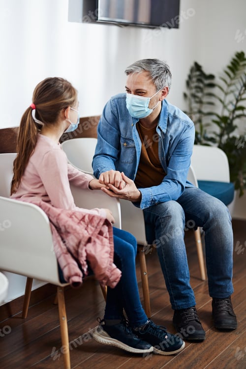 Visualização: Pai sorridente segurando a mão da filha enquanto conversava na sala de espera do consultório médico.