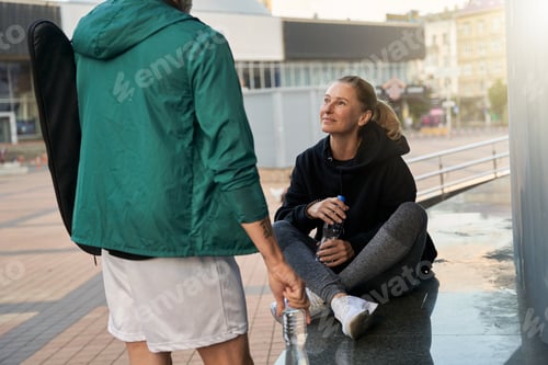 Preview: Sportive mature woman woman in sportswear talking with her partner outdoors while waiting together