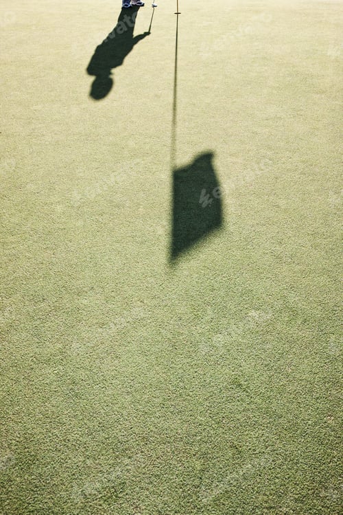 Preview: Shadow of a golfer and a flag on a golf green.