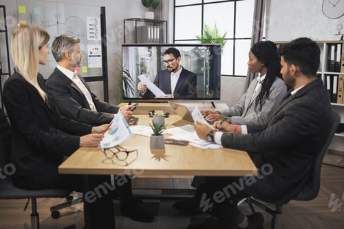 Preview: Team of four focused multiethnical businesspeople looking at screen, having video conference