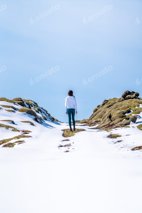 Preview: Woman with her back on a snowy road on a sunny day in Iceland