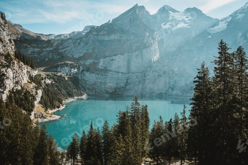 Preview: Lake surrounded by rocks covered in the snow and forests under the sunlight
