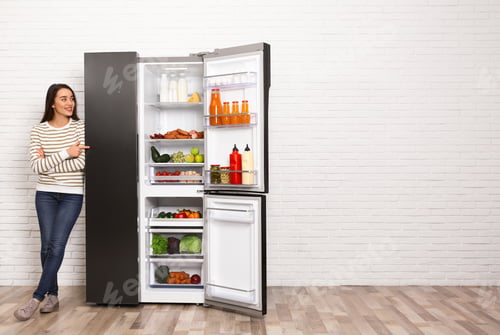 Preview: Happy young woman near open refrigerator indoors, space for text