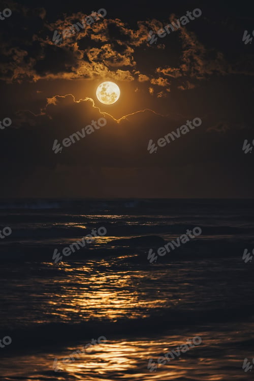 Preview: Big moon between the clouds over the ocean. Moon light on the water in the night.