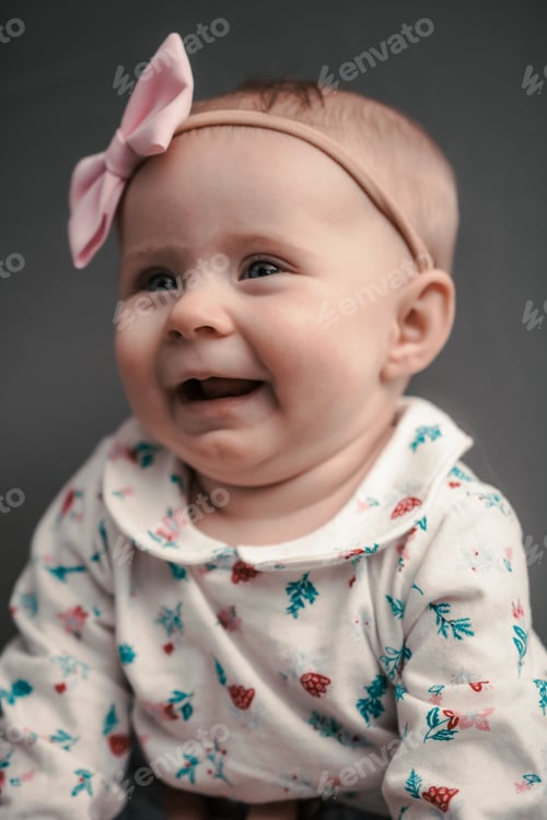 Preview: Vertical shot of an adorable baby in a cute shirt and a pink bow