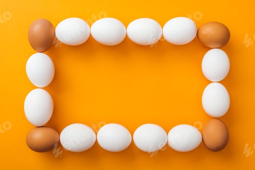 Preview: top view of whole white and brown organic chicken eggs arranged in square frame on bright orange