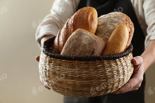 Preview: Man holding wicker basket with different types of bread on beige background, closeup