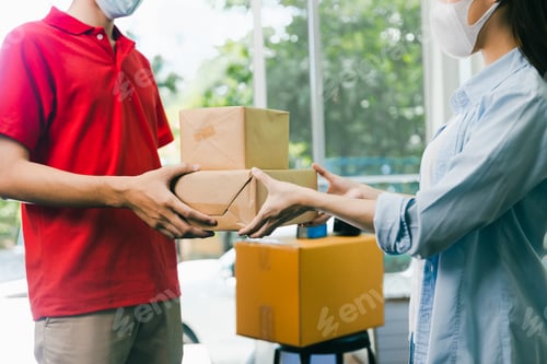 Preview: Asian delivery man wearing face mask in red uniform deliver service parcel box to woman customer