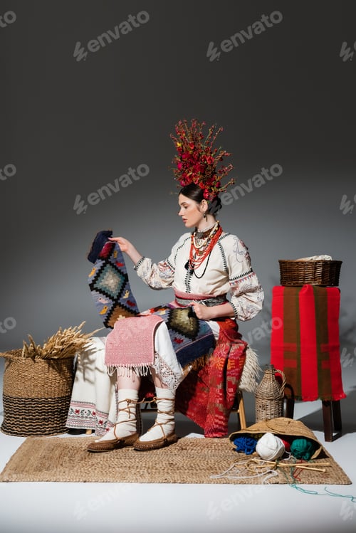 Preview: full length of young ukrainian woman in traditional clothes and red floral wreath holding knitted