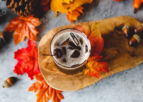 Preview: Flat-lay with whiskey drink with cherry, fall autumn orange and red leaves, acorns and a wooden slab