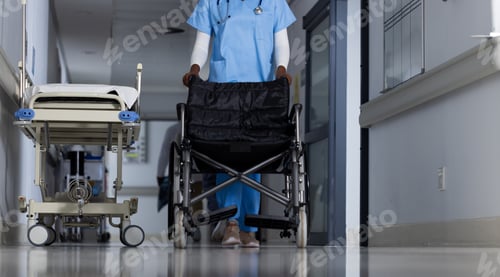 Preview: Midsection of african american female doctor walking with wheelchair in corridor at hospital
