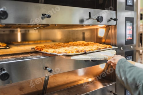 Preview: Baker taking freshly baked pastries out of oven in a bakery
