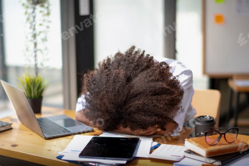 Preview: A woman with curly hair is sleeping on a desk with a laptop, a tablet