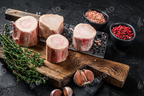 Preview: Uncooked Raw veal Marrow bones on butcher board with meat cleaver. Black background. Top view