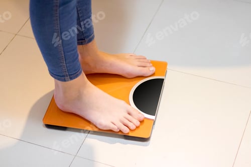 Preview: Low section of woman checking her weight on weighing scales at home