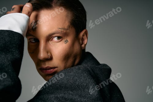 Preview: Young and attractive person with tattoos poses elegantly in a stylish outfit against a dark backdrop