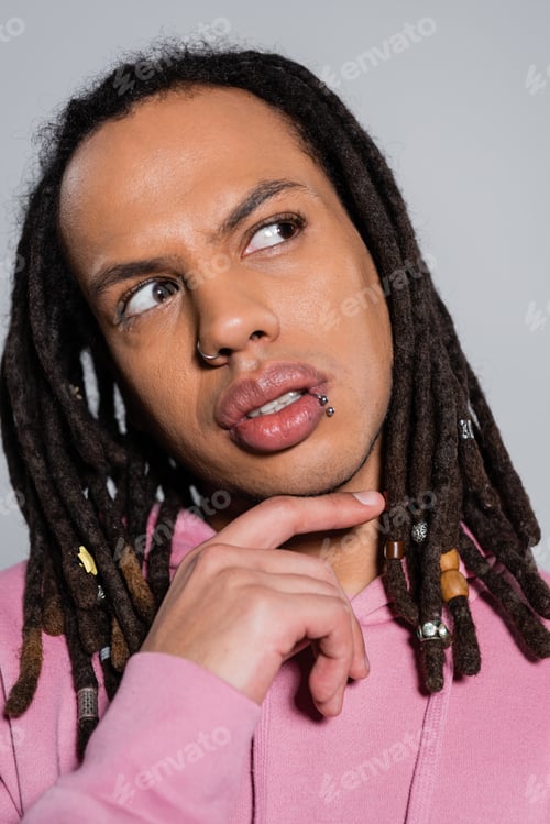 Preview: portrait of pensive multiracial man in pink hoodie looking away isolated on gray