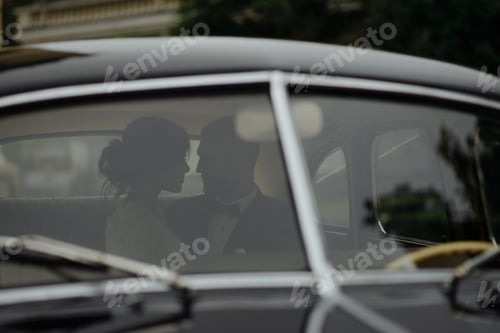 Preview: Beautiful happy young bride and groom looking from retro auto