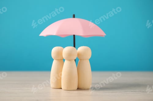 Preview: Human figures under umbrella on wooden table against light blue background. Insurance concept