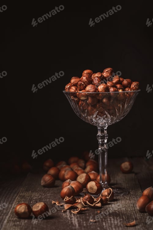 Preview: close up view of shelled hazelnuts in glassware on wooden surface on black background